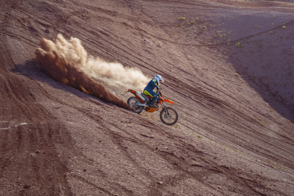 Dirt bike rider on a KTM bike descending a sandy hill at Sand Hollow, Utah, near Zion, creating a dust trail.